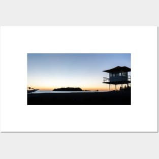 Silhouetted against golden glow of sunrise lifesafers lookout on Mount Maunganui beach New Zealand. Posters and Art